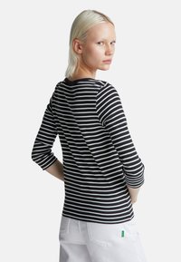 Czarna i biała w paski koszula z długim rękawem, okrągłym dekoltem, dopasowanym krojem i lekko rozkloszowanym dołem, w zestawieniu z białymi spodniami.