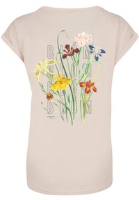 Light pink T-shirt with short sleeves featuring a floral graphic pattern in multiple colors and the text "BLÖM" integrated into the design.