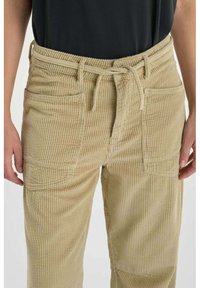 Beige corduroy broek met een geribbelde textuur, voorzien van een trekkoord in de taille en twee broekzakken aan de voorkant.
