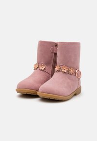 Pink faux leather ankle boots with a side zipper, floral embellishment, and a beige rubber sole. Features a decorative strap with a buckle.