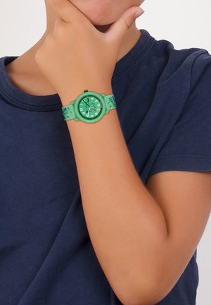 Grön silikonklocka med en cirkulär urtavla, som har en grön urtavla och vita siffror. Armbandet har lekfulla mönster i en matchande grön nyans.