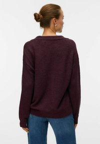 Maglione oversize borgogna con collo a camicia, polsini a coste e texture morbida, abbinato a jeans in denim blu.