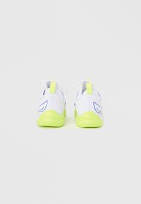 Ζευγάρι λευκά αθλητικά παπούτσια με φωσφορίζουσες κίτρινες σόλες και ταμπέλες στη φτέρνα, απεικονισμένα από πίσω σε λευκό απλό φόντο.