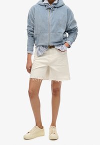 Sudadera con capucha de color azul claro y cremallera, pantalones cortos de mezclilla beige deshilachados y zapatillas de crema. Rayas horizontales visibles en la camiseta de abajo.