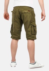 Olivgrüne Cargo-Shorts mit mehreren Taschen, lockerer Passform und knielangem Design. Getragen mit weißen Sneakern. Baumwollmaterial.