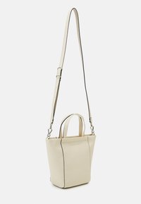 Mała torebka tote w kolorze kremowym, wykonana z materiału syntetycznego, z krótkimi uchwytami, długim regulowanym paskiem i kontrastującym czarnym przeszyciem.