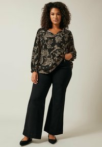Blusa nera floreale con maniche lunghe e scollo a V, abbinata a pantaloni neri a gamba larga e décolleté neri a punta. Tessuto testurizzato con un motivo dorato.