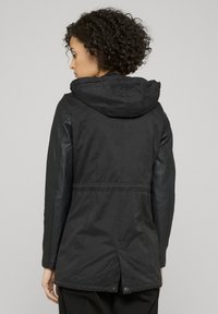 Svart jacka med huva, åtsittande midja och rak skärning i standardlängd. Materialmix med glansig finish på ärmarna.