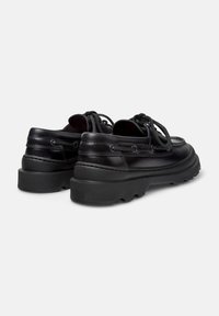 Black leather shoes with a rounded toe, textured finish, thick black sole, and contrasting lace accents on the sides.