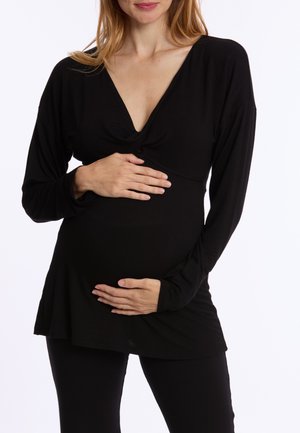 Zwart langslurf top met een diepe V-hals, een getailleerd ontwerp en zachte stof, gedragen over een ronde buik; gecombineerd met zwarte leggings.