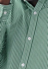 Zielona i biała, w poziome paski koszula wykonana z bawełny, z klasycznym kołnierzykiem, białymi guzikami i pionowymi paskami.
