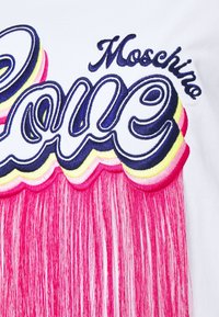 Witte stof met "Love" in vette, marineblauwe borduursel en gelaagde roze en gele franjes eronder. Opvallende ontwerpelementen zijn de levendige kleurcontrasten.