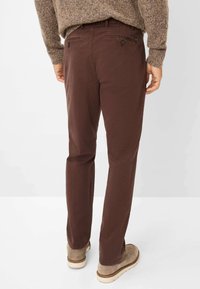 Braune Baumwollhosen mit geradem Schnitt, ausgestattet mit zwei Gesäßtaschen und Knopfverschlüssen, getragen mit beigen Wildlederschuhen.
