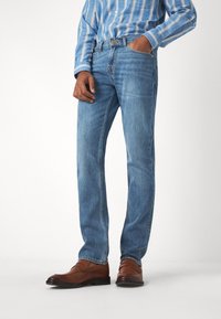 Jeans in denim azzurro chiaro con una vestibilità dritta, caratterizzati da un classico design a cinque tasche e sbiaditure delicate. Abbinati a scarpe in pelle marrone.