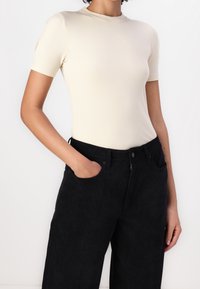 Beżowa, prążkowana bluzka z krótkim rękawem i wysokim dekoltem, zestawiona z czarnymi spodniami z kordurowej tkaniny z szerokimi nogawkami, z kieszeniami z przodu i zamek błyskawiczny.