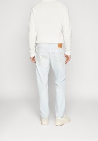 Jeans de mezclilla azul claro con corte recto, detalles de costura mínimos, dos bolsillos traseros y un parche de cuero marrón en la cinturilla.