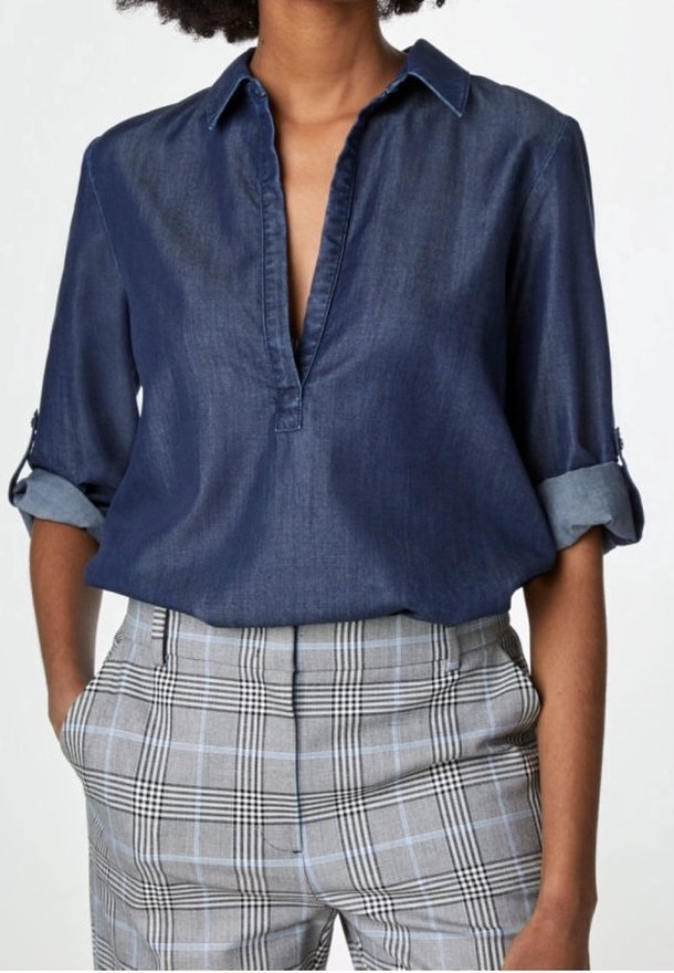 Femme portant un chemisier bleu marine à manches longues avec manches retroussées et un pantalon taille haute à carreaux gris, mains dans les poches.