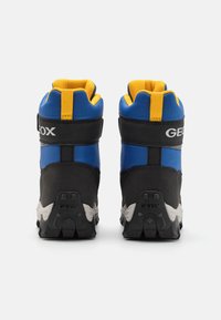 Une paire de chaussures de randonnée noires et bleues avec des cols rembourrés jaunes, des semelles noires et un logo "GEOX" sur le talon et la sangle, vue de l'arrière.
