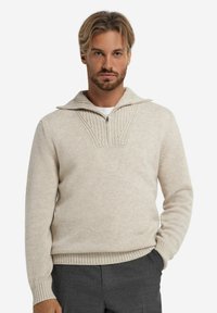 Beige Wolle Pullover mit halbem Reißverschlusskragen, strukturiertem Strickdetail an der Vorderseite, gerippten Bündchen und Saum. Figurbetonter Schnitt.