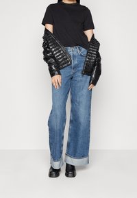 Svart t-shirt i kombination med en glänsande svart puffjacka, vida blå jeans med uppvikt nederkant och svarta ankelstövlar.