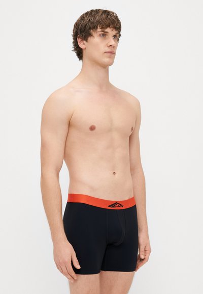 Juodi bokseriai su oranžiniu liemeniu ir prekės ženklu. Audinys atrodo lygus ir patogiai prigludęs, sukurtas komfortui.