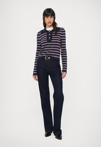 Marineblauw-wit gestreept shirt met lange mouwen, een kraag en een knoopsluiting, gecombineerd met donkerblauwe uitlopende jeans en een gouden riem.