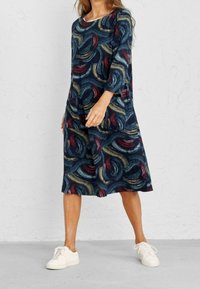 Laivansinis mekko, jossa on punaisella, vihreällä ja keltaisella swirl-kuviointi. Valmistettu pehmeästä, teksturoidusta kankaasta, jossa on kolmanneksen hihat ja taskut.