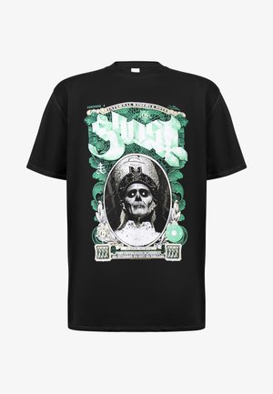 Camiseta negra con un estampado gráfico de una figura esquelética que lleva una corona, rodeada de un diseño ornamental verde y elementos de billetes de dólar.