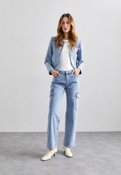 Lys blå denimjakke med sølvknapper, kombinert med lys blå cargo-bukser med sidelommer og en hvit ribbestrikket topp. Kremfargede ankelstøvler.