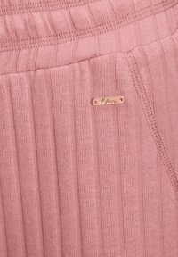 Roze ribbeltextiel met een klein, rechthoekig metalen logo-label met de tekst "s.Oliver." Gelaagd materiaal met horizontale lijnen.