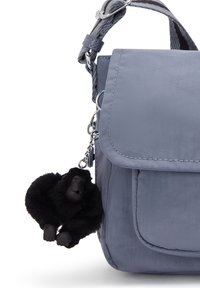 Borsa a tracolla in tessuto grigio con tasca frontale e portachiavi a forma di gorilla peloso nero attaccato all'anello della tracolla.