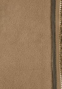 Rjavo flisasto blago z mehkimi teksturami. Na eni strani je viden kontrastni rob z zadrgo, z zlatim okovjem in temno tkanino oblogo.