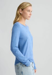 Hellblauer Pullover mit langen Ärmeln, rundem Halsausschnitt und strukturiertem Muster aus kleinen Kreisen. Aus weichem Strickstoff gefertigt.