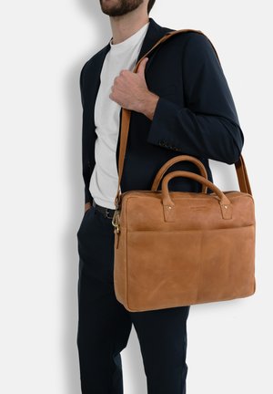 Braune Leder-Umhängetasche mit zwei Griffen und einem langen Riemen, glatt in der Textur und mit minimalistischem Design, geeignet für den professionellen Gebrauch.