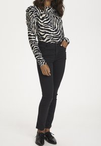 Schwarze Jeans kombiniert mit einem langärmligen Oberteil mit einem cremefarbenen und schwarzen Zebra-Print, mit gerafften Ärmeln und einem runden Ausschnitt.