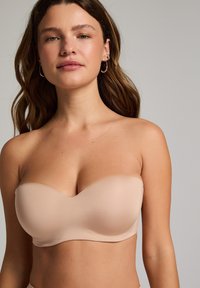 Hautfarbener, trägerloser BH aus glattem Stoff, leicht gepolstert, mit einem geschwungenen Ausschnitt und nahtlosem Design, das die klassische Bandeau-Form aufweist.