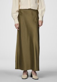 Jupe maxi en satin vert olive avec une texture lisse, une coupe droite et un léger éclat, associée à des chaussures à talons blocs crème.