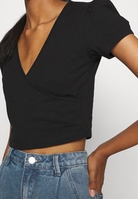 Haut noir court avec un design en V, manches bouffantes courtes et en coton lisse, associé à un short en denim taille haute.