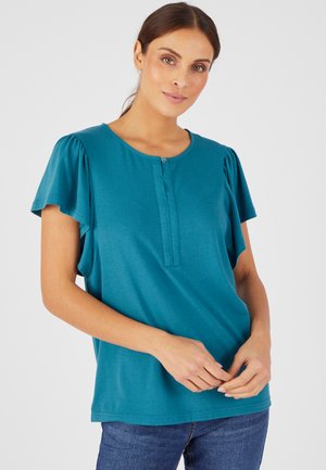 Top teal à manches courtes avec un col rond, présentant une patte de boutonnage et des manches froncées. Fabriqué en tissu doux et léger.