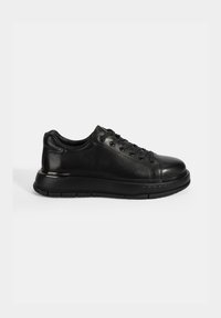 Sneaker en cuir noir avec un bout arrondi, un design à lacets et une semelle en caoutchouc épaisse. Présente une texture lisse et élégante avec des accents légèrement brillants.