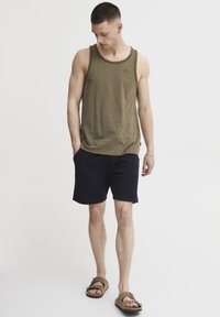 Olivengrünes Tanktop mit geripptem Halsausschnitt, kombiniert mit schwarzen Shorts. Flache Sandalen runden das Outfit ab und betonen entspannte Sommermode.