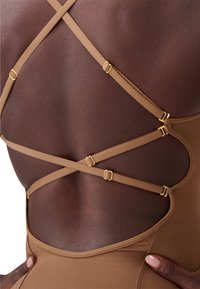 Bruine bodysuit met een ontwerp met straps op de rug, voorzien van gouden hardwareaccenten. Soepele textuur met uitsnijdingen aan de zijkanten.
