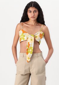 Top corto floreale in crema, arancio e verde con un nodo davanti. Spalline sottili e design aderente. Tessuto dalla trama liscia.