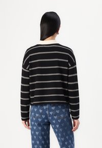 Black striped sweater with white horizontal lines, rounded neckline, soft fabric, and cropped cut, worn over light blue heart-patterned jeans.