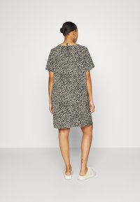 Robe à manches courtes beige avec des taches de léopard noires, dotée d'un col rond et d'une découpe en forme de clé au dos. Portée avec des chaussures claires.
