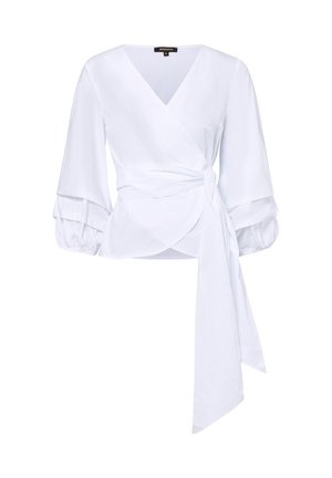 Blouse portefeuille blanche avec col en V, manches longues bouffantes avec poignets à volants et longue ceinture nouée à la taille.