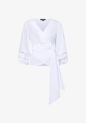 Blouse portefeuille blanche avec col en V, manches longues bouffantes avec poignets à volants et longue ceinture nouée à la taille.