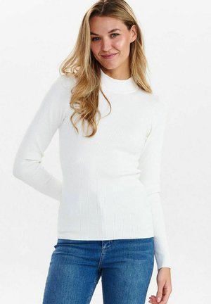 Bijela rebrasta dugački rukav turtleneck majica s prilagođenim siluetom, uparena s plavim trapericama. Glatka textura i jednostavan dizajn.