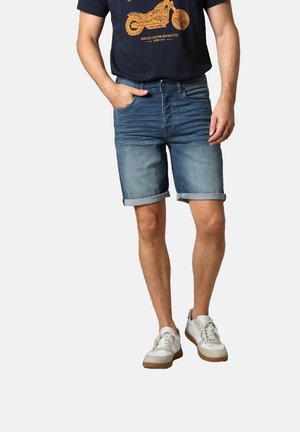 Shorts en denim de bleu clair à moyen, avec un ourlet retroussé, associés à un t-shirt navy foncé avec un imprimé graphique orange. Baskets blanches décontractées.