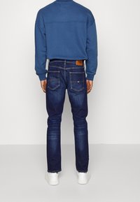 Mörkblå denimjeans med rak passform, utrustade med två bakfickor, subtila sömnadsdetaljer och en logotyp i brunt läder vid midjan.